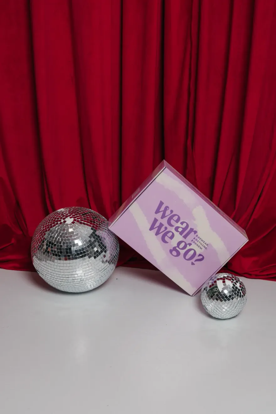 Pudełko WearWeGo i kule disco na tle czerwonej kurtyny